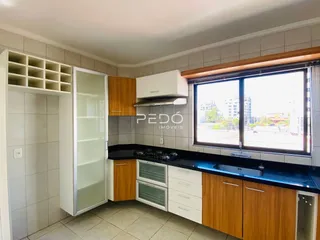Vista da cozinha com armários de madeira e bancadas escuras.