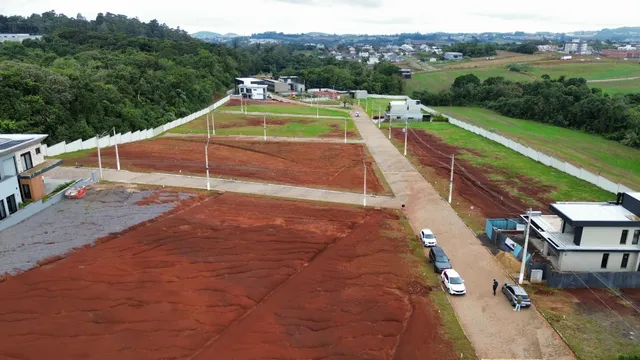 Vista aérea de um terreno grande e não construído com solo avermelhado e áreas gramadas.