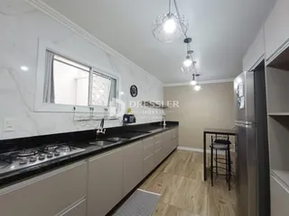 Vista da cozinha com armários brancos e bancadas escuras.