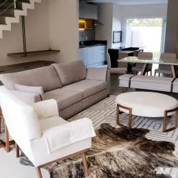 Sala de estar com sofá e poltronas brancas em um ambiente bem iluminado.
