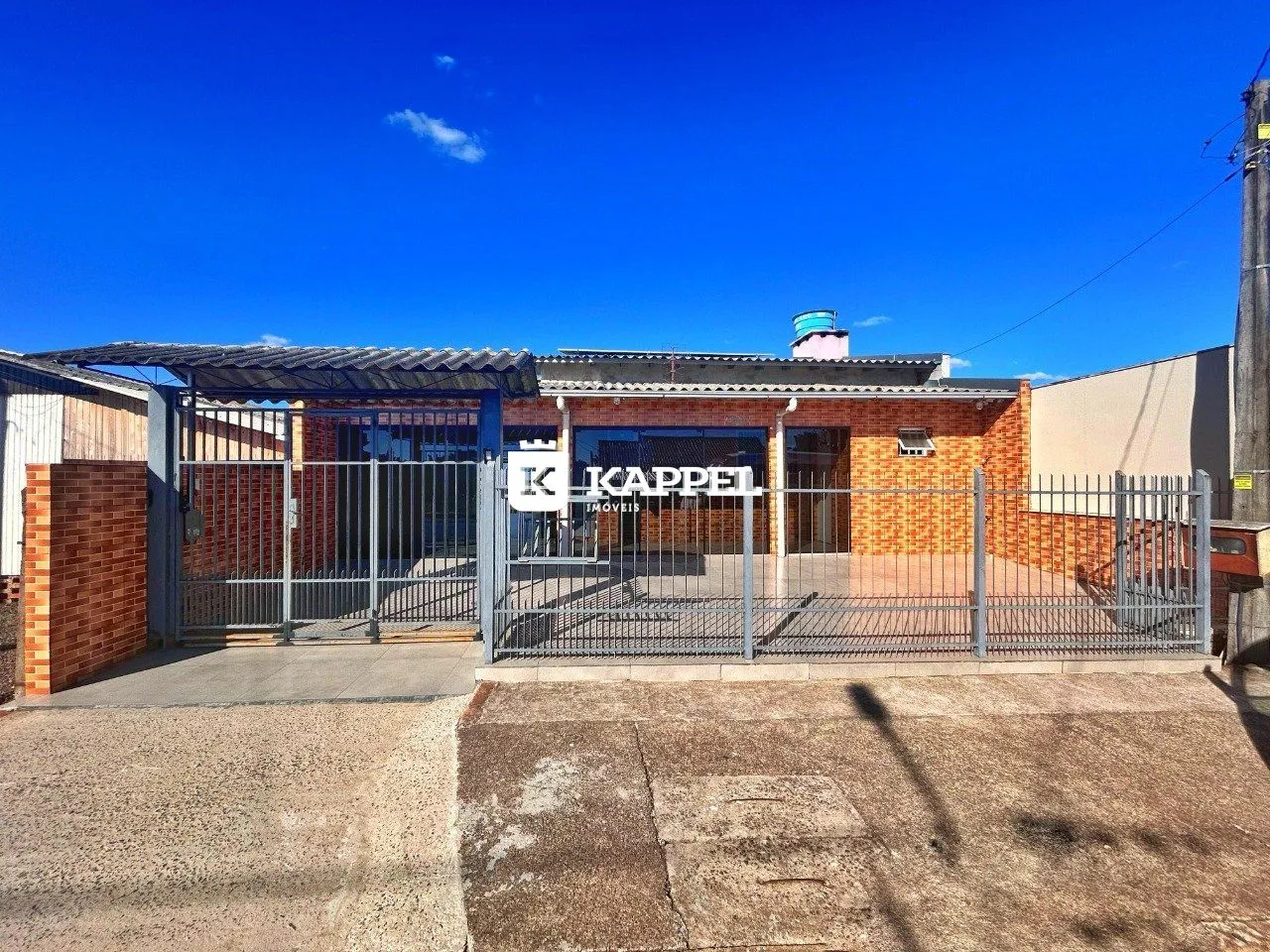 Vista externa de uma residência com fachada de tijolos vermelhos e cerca de metal.