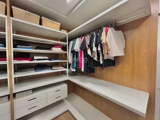 Armário e prateleiras brancas com roupas penduradas em um ambiente interno.