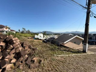 Foto externa mostrando um terreno com materiais de construção e uma vista de colinas ao fundo.