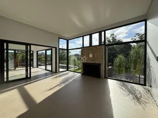 Ambiente interno de uma sala ampla com grandes janelas e lareira de pedra.