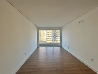 Interior de uma sala com piso de madeira e vista para o exterior.