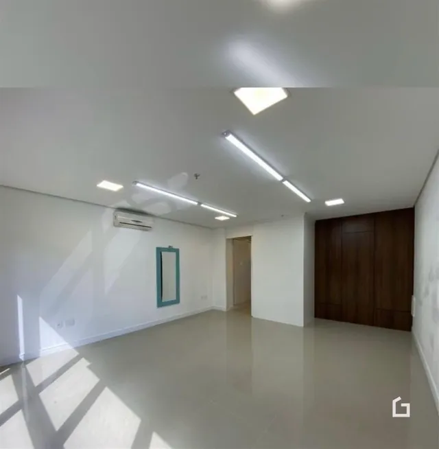 Ambiente interno de uma sala ampla com paredes brancas e piso claro.