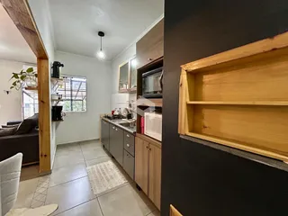 Ambiente interno de sala de estar e cozinha com piso de cerâmica e armários de madeira.