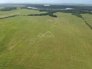 Vista aérea de uma área rural com campos verdes e um rio ao fundo.