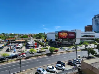 Vista externa de um edifício com uma rua movimentada e um estabelecimento comercial ao fundo.