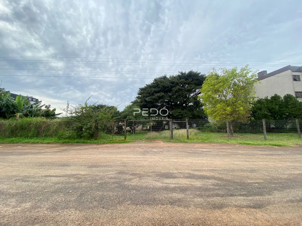 Vista externa da propriedade com cerca e vegetação ao fundo.