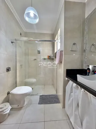 Foto de um banheiro com box de vidro e piso de cerâmica branca.