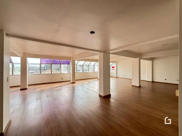 Uma sala de estar ampla com piso de madeira clara e pé direito alto.