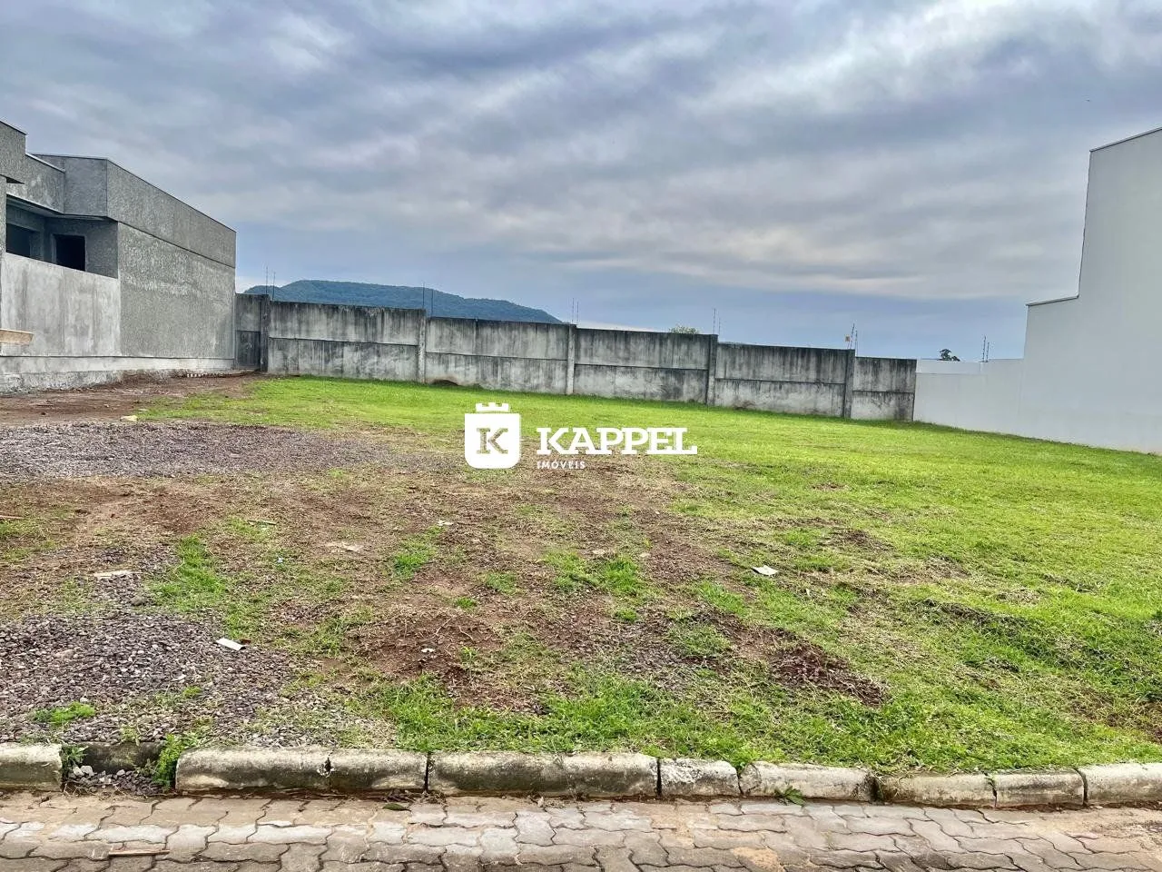 Vista externa de um terreno com grama seca e muros de concreto.
