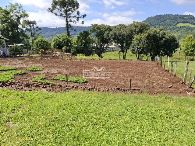Campo aberto com vegetação e cerca de madeira em uma paisagem montanhosa.