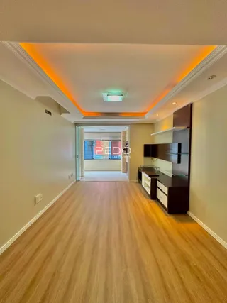 Corredor interno de uma residência com piso de madeira clara e iluminação embutida.