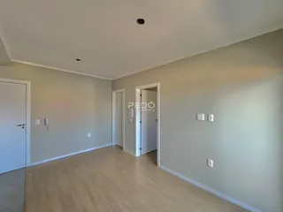 Vista interna de uma sala com piso de madeira clara e paredes neutras.