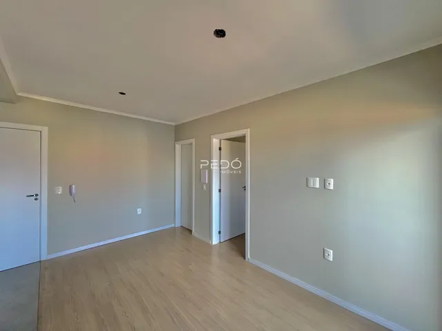 Vista interna de uma sala com piso de madeira clara e paredes neutras.