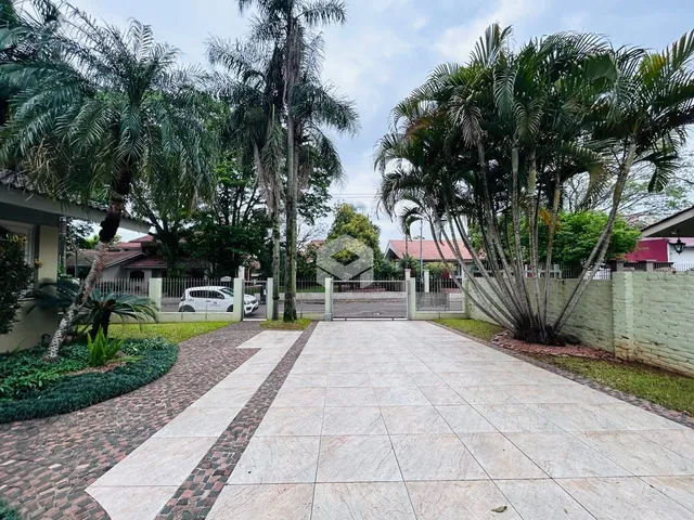 Vista da entrada de uma propriedade com paisagismo e calçada de pedras.