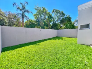 Gramado verde com muro branco e vegetação ao fundo.