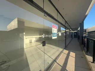 A foto mostra um corredor interno com piso de cerâmica e paredes de vidro.