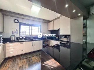 A cozinha moderna apresenta armários brancos e bancadas escuras.