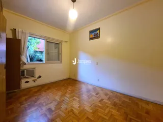 A sala de estar apresenta piso de madeira e uma janela com venezianas brancas.