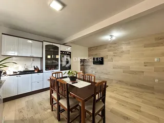 Sala de jantar e cozinha com armários brancos e piso de madeira clara.
