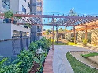 Vista externa de um pátio com pergolado e jardim.