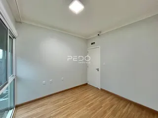 Interior de uma sala com piso de madeira clara e paredes brancas.