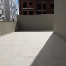 Vista de uma área externa pavimentada com piso claro.