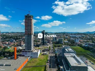 Vista aérea de um desenvolvimento urbano com um arranha-céu em construção e áreas verdes.