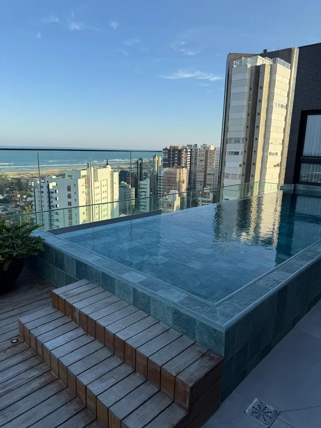 Piscina com deck de madeira e vista para o mar.