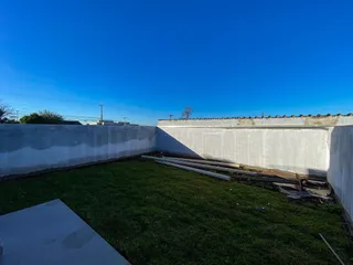 Vista externa mostrando um gramado e um muro branco em uma propriedade.