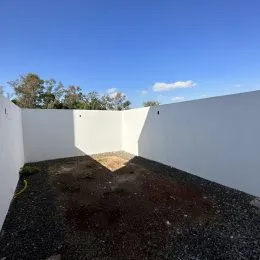 Vista externa de um terreno com muro branco e solo de cascalho escuro.