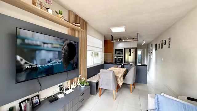 Sala de estar com televisão e área de cozinha visível.