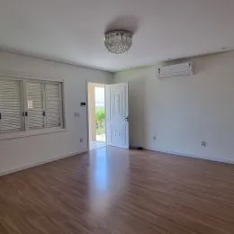 Sala de estar ampla com piso de madeira clara e paredes brancas.