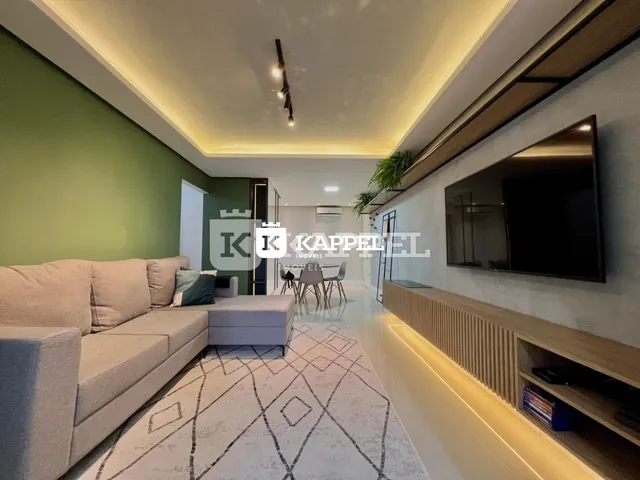 Sala de estar com sofá claro e televisão montada na parede.