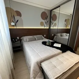 Quarto com cama e piso de madeira clara em um imóvel.
