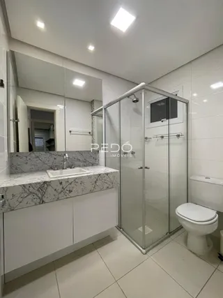 Interior de um banheiro com revestimento de mármore e box de vidro.