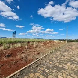 Vista de uma área externa com caminho de pedra em um campo aberto sob um céu azul e nuvens.