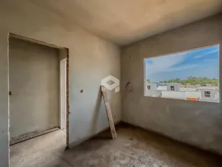 Interior de um cômodo com paredes em obra e uma janela com vista para o horizonte.
