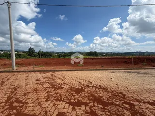 Paisagem de terra vermelha com vegetação ao fundo sob um céu azul.