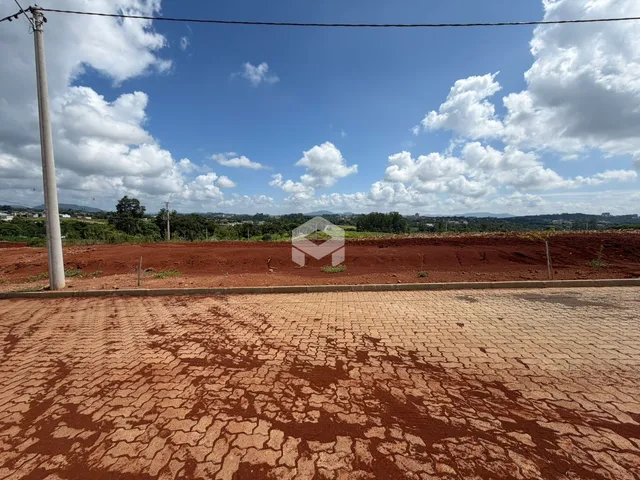Paisagem de terra vermelha com vegetação ao fundo sob um céu azul.