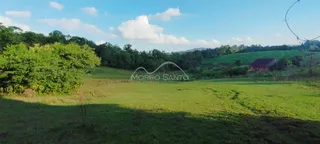 Vista panorâmica de um campo verde com vegetação ao fundo.