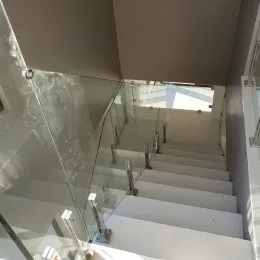 Vista de um corredor com guarda-corpos de vidro e escadaria.