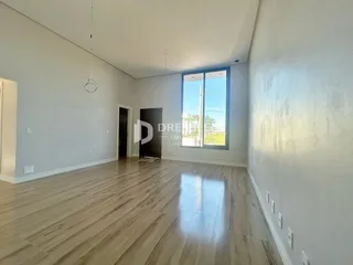 Ambiente interno de uma sala ampla com piso de madeira clara e grande janela.