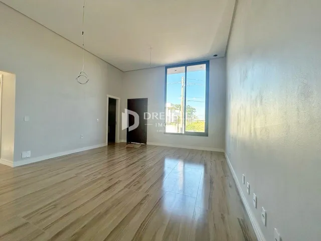 Ambiente interno de uma sala ampla com piso de madeira clara e grande janela.
