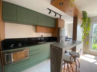 Cozinha com armários verdes, bancadas escuras e ilha de pedra.