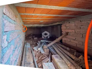 Imagem de uma área interna em construção com paredes de tijolo expostas e entulho.