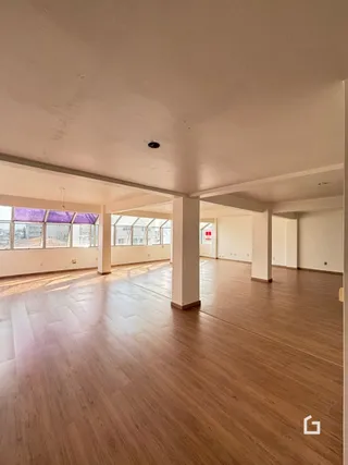 Vista interna de um ambiente com piso de madeira clara e colunas brancas.